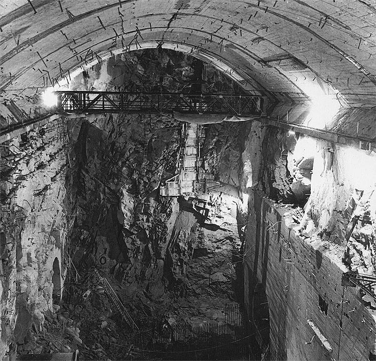 Vodní elektrárna Lipno, Lipno I - Elektrárna, pohled od šikmého tunelu na čelní stěnu s poruchovou zónou. Výlom jádra dokončen, na konzolách klenby pojíždí montážní jeřáb 5 t., vpravo vybetonovaný portál odpadů, duben 1958, historické foto